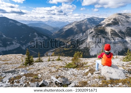 Young Boy sitting on a rock overlooking a mountain vally in the Canadian Rockies at Moose Mountain Kananaskis Alberta.