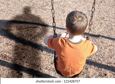 A young boy is sitting on a swing set and looking at a shadow figure of a man or bully at a playground. Use it for a kidnap, defense or safety concept.