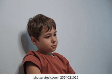 A young boy sitting quietly with a thoughtful expression, leaning against a light-colored wall. His pose suggests deep contemplation or introspection. - Powered by Shutterstock