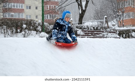 Young boy sleds down a snowy hill, his face lit up with pure joy. The slow-motion effect adds to the sense of wonder, capturing the magic of a winter wonderland. - Powered by Shutterstock