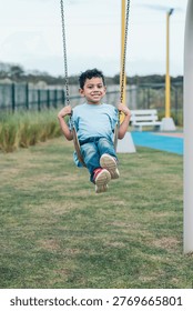 Young boy smiling at the camera while swinging on a playground, having fun and enjoying the outdoor activity