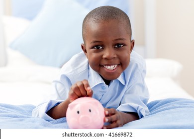 Young Boy Smiling At The Camera While Putting Money Into His Piggy Bank