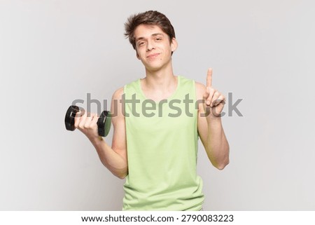 young boy smiling and looking friendly, showing number one or first with hand forward, counting down. dumbbell concept