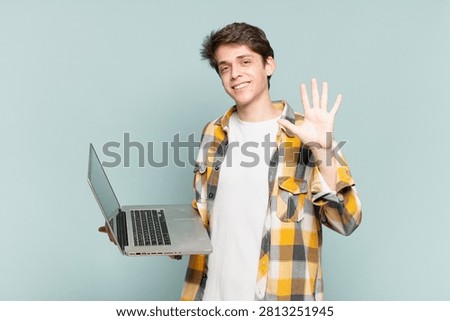 young boy smiling and looking friendly, showing number five or fifth with hand forward, counting down. laptop concept