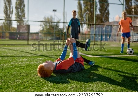 Young boy soccer player with injured knee lying on field