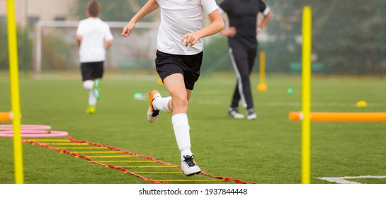 Young Boy In Soccer Shoes Cleats Running Through Training Ladder. Coach In The Background. Football Agility Training For Youth Soccer Club