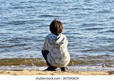 Young Boy Squatting Next To Ocean Shore