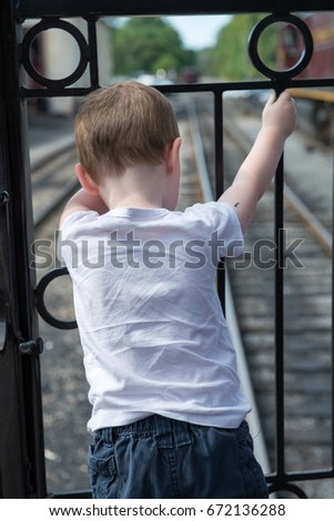 Young boy standing at back of train looking down at track