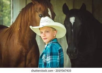 A young boy standing in front of some horses with a cowboy hat on looking back