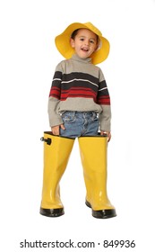 Young Boy Standing In Large Yellow Rain Boots And A Yellow Rain Hat Isolated On White