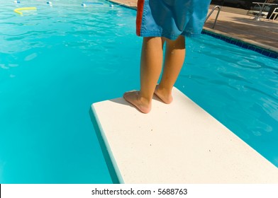 Young boy standing on the end of a diving board at a swimming pool - seems to be a little apprehension
