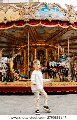 Young boy standing and smiling in front of the illuminated vintage carousel in piazza della repubblica
