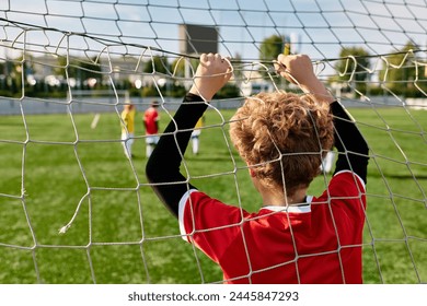 A young boy stands confidently in front of a soccer net, ready to defend against any incoming shots with determination and focus. - Powered by Shutterstock