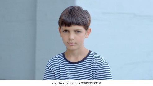 Young boy in striped shirt making direct eye contact with the camera. Use of natural lighting suggests soft and authentic quality of visual image. Intimate and engaging lifestyle portrait of teenager.
