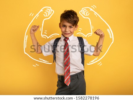 Young boy student acts like a muscled man. Yellow background