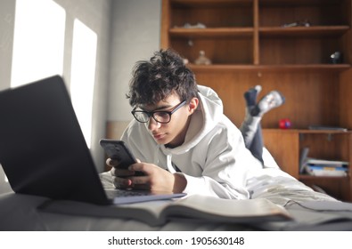 Junge Junge lernt mit Computer und Smartphone auf dem Bett liegen
