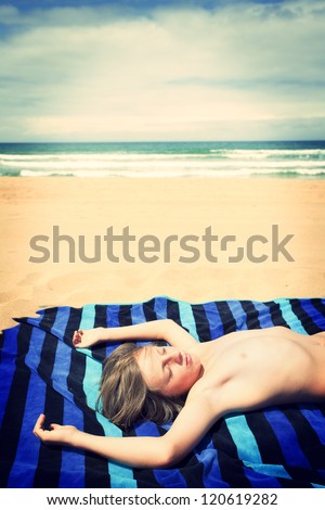 Young boy sunbathing on the beach. Cross procesing effects.