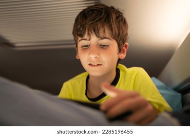 Young boy with tablet in motorhome on road trip vacations. Kid enjoying in camper indoor parked on a campsite at night. Shining through the window. Active family holidays. - Powered by Shutterstock