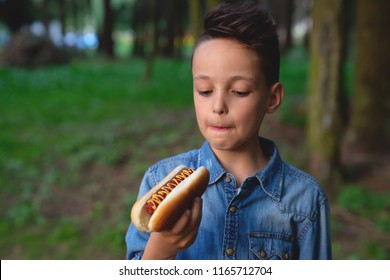 A Young Boy Takes A Bite Of A Hot Dog In Park