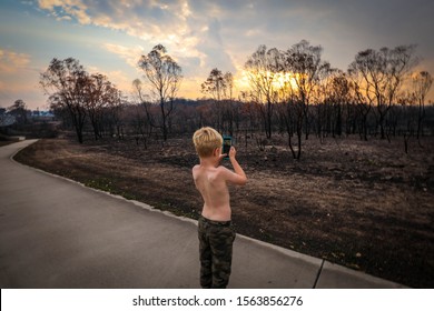 Young Boy Taking Photos Of Land Burnt Out By Bush Fires In New South Wales, Australia