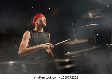 young boy as talented rock band drummer . Handsome and cool Asian American teenager in headband playing drum kit performing night music show as hobby in teenage  love for music 