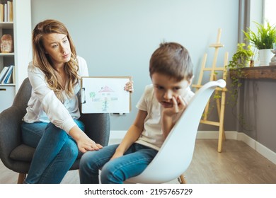 Young Boy Talking With Counselor At Home. Female Psychologist Working With Little Boy In Office. Young Female School Psychologist Having Serious Conversation With Smart Little Boy