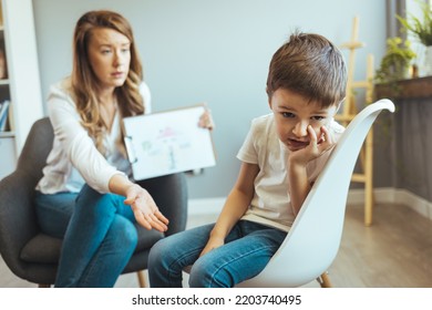 Young Boy Talking With Counselor At Home. Female Psychologist Working With Little Boy In Office. Young Female School Psychologist Having Serious Conversation With Smart Little Boy