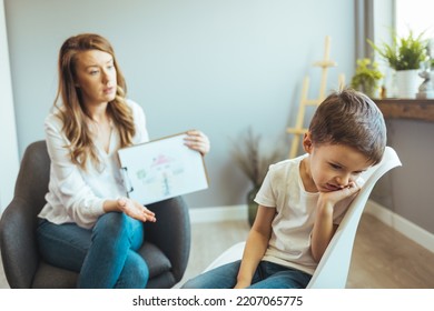 Young Boy Talking With Counselor At Home. Female Psychologist Working With Little Boy In Office. Young Female School Psychologist Having Serious Conversation With Smart Little Boy