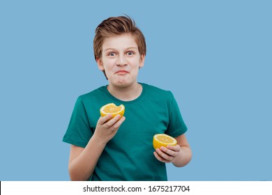 Young Boy Taste A Fresh Lemon, Sour Taste, Make Grimace, Facial Emotions Negative, In Green T-shirt Isolated On Blue Background, Copy Space