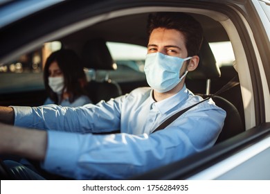 Young Boy Taxi Driver Gives Passenger A Ride Wearing Sterile Medical Mask. A Man In The Car Behind The Steering Wheel Works During Coronavirus Pandemic. Social Distance And Health Safety Concept.