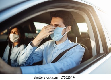 Young Boy Taxi Driver Gives Passenger A Ride And Adjusts Sterile Medical Mask. A Man In The Car Behind The Steering Wheel Works During Coronavirus Pandemic. Social Distance And Health Safety Concept.