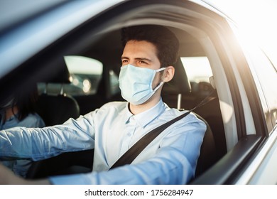 Young Boy Taxi Driver Gives Passenger A Ride Wearing Sterile Medical Mask. A Man In The Car Behind The Steering Wheel Works During Coronavirus Pandemic. Social Distance And Health Safety Concept.