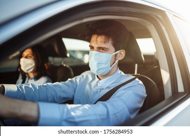 Young Boy Taxi Driver Gives Passenger A Ride Wearing Sterile Medical Mask. A Man In The Car Behind The Steering Wheel Works During Coronavirus Pandemic. Social Distance And Health Safety Concept.