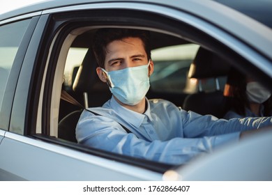 Young Boy Taxi Driver Gives Passenger A Ride Wearing Sterile Medical Mask. A Man In The Car Behind The Steering Wheel Works During Coronavirus Pandemic. Social Distance And Health Safety Concept.