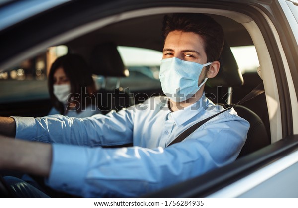 Young boy taxi driver gives passenger a ride\
wearing sterile medical mask. A man in the car behind the steering\
wheel works during coronavirus pandemic. Social distance and health\
safety concept.