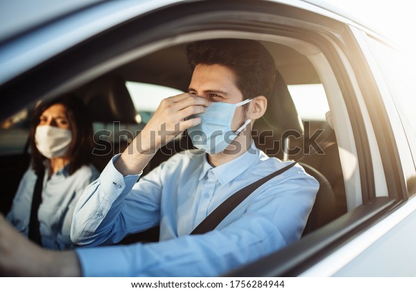Young boy taxi driver gives passenger a ride and\
adjusts sterile medical mask. A man in the car behind the steering\
wheel works during coronavirus pandemic. Social distance and health\
safety concept.