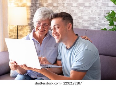 Young boy teaching his grandmother how to surf the internet, buy products online while holding the laptop and together watching a video - Powered by Shutterstock