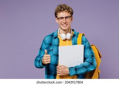 Young boy teen student in casual clothes backpack headphones glasses hold folder papers document show thumb up isolated on violet background studio Education in high school university college concept