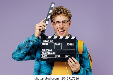 Young boy teen student in casual clothes backpack headphones glasses hold classic black film make clapperboard isolated on violet background studio Education in high school university college concept