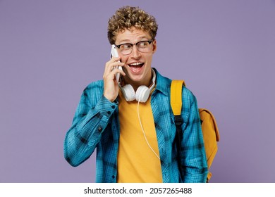 Young Boy Teen Student In Casual Clothes Backpack Headphones Glasses Talk Mobile Cell Phone Isolated On Plain Pastel Light Violet Background Studio. Education In High School University College Concept