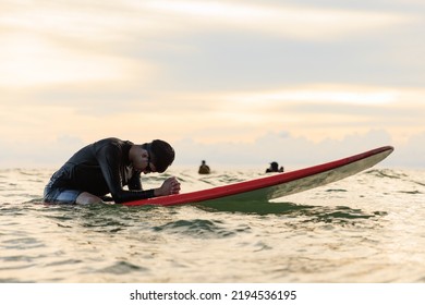 Young boy teenager surfboarder bows his head in exhaustion, tired, and disappointment during learning and practicing surfing. Concept for failing training, pause, and trying to fight again.