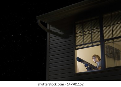 Young Boy With Telescope At Open Window Looking At Night Sky