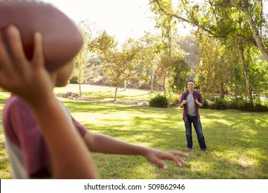 Young Boy Throwing American Football To His Dad In Park