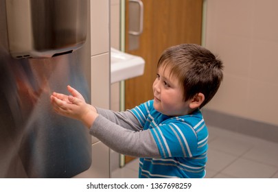 A Young Boy Uses A Air Hand Dryer To Dry His Hands After Washing Them In The Bathroom Sink.