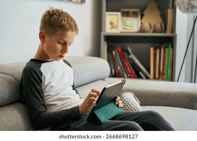 Young boy using digital tablet on sofa at home