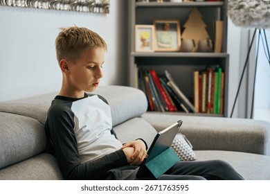 Young boy using digital tablet on sofa at home