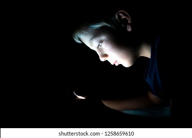 Young Boy Using His Smartphone Late At Night Alone In The Dark. Light Shining On His Face.