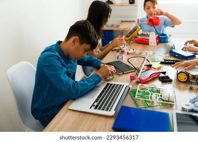 Young boy using a laptop and coding while learning and building a robot during his electronics course school