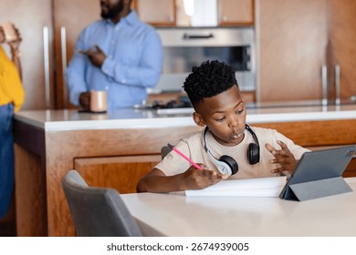 Young boy using tablet and writing in notebook at home, focused on learning. Studying, education, technology, homework, concentration, child