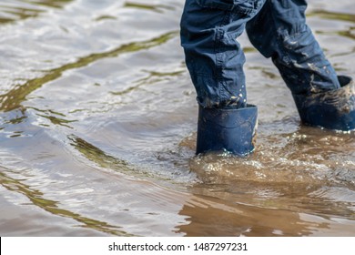 Young Boy Wading Through High Tide With Blue Gumboots After A Flood Has Broken The Protecting Dike And Overflowing The Netherlands